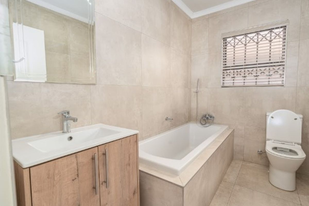 A modern, neutral-toned bathroom featuring a built-in bathtub, vanity cabinet with basin, and a toilet, finished with floor-to-ceiling wall tiles.