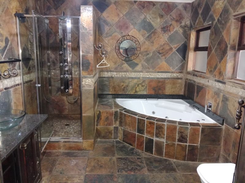 A spacious bathroom featuring a corner spa bath, a walk-in shower with a modern panel, and extensive slate tile finishes throughout.