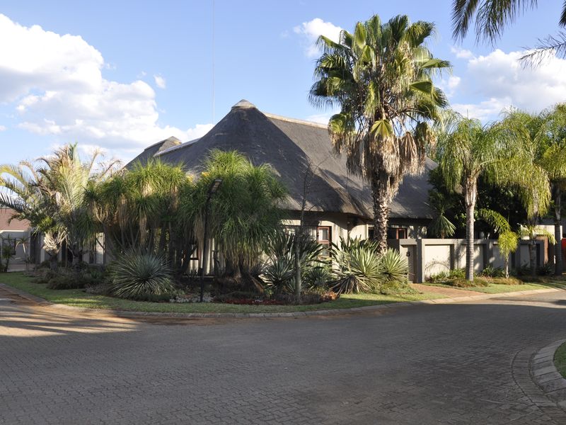 A well-maintained residential property featuring a traditional thatched roof, established garden, and paved driveway, situated on a corner lot.