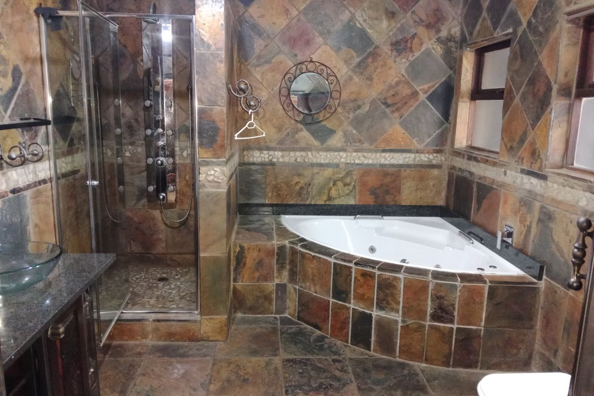 A spacious bathroom featuring a corner spa bath, a walk-in shower with a modern panel, and extensive slate tile finishes throughout.