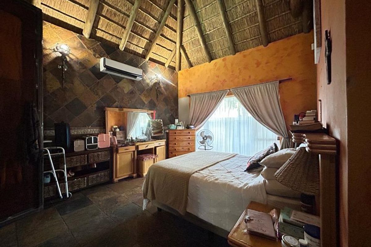 A rustic bedroom featuring a high thatched ceiling with exposed timber rafters, slate tile flooring, and a feature slate wall.