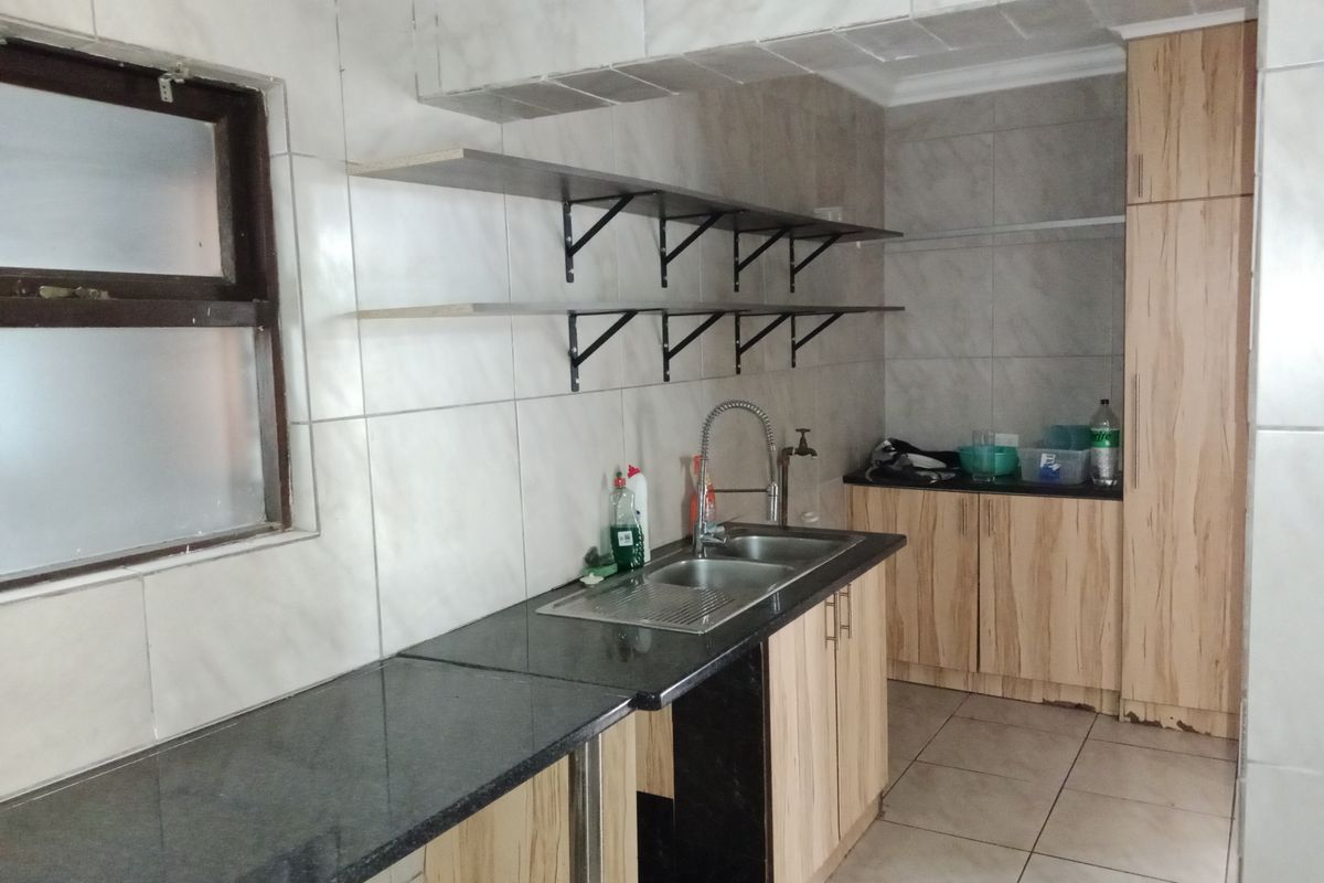 A functional kitchen featuring granite countertops, double sink, built-in cabinetry, and open shelving with tiled wall finishes.
