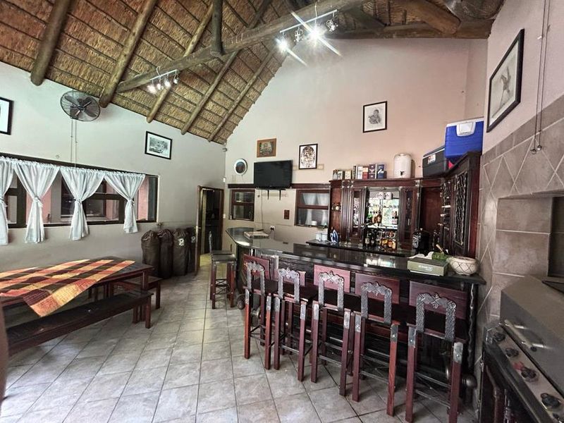 Spacious entertainment area featuring a built-in bar, tiled flooring, and a high thatched roof with exposed timber rafters, perfect for hosting guests.
