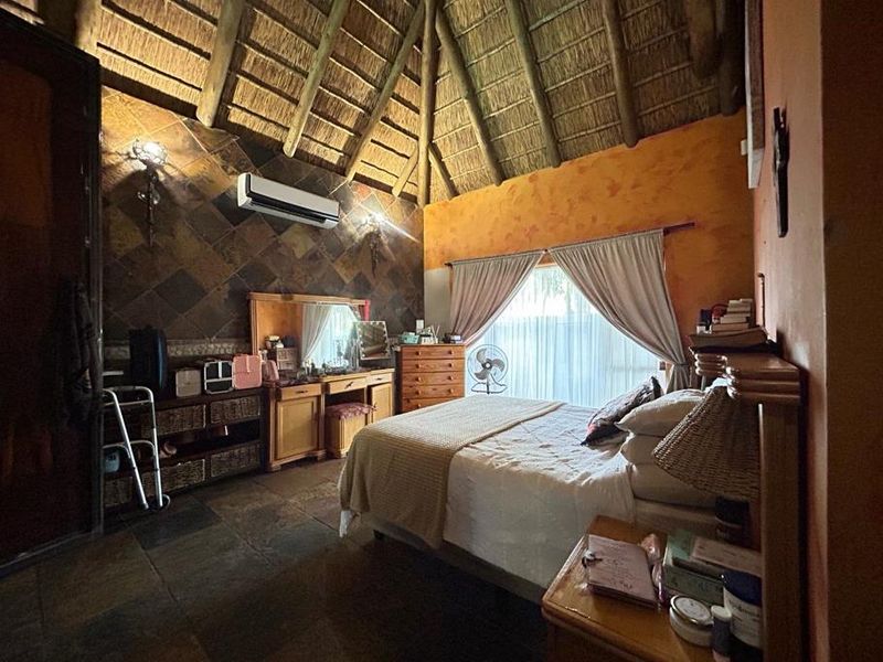 A rustic bedroom featuring a high thatched ceiling with exposed timber rafters, slate tile flooring, and a feature slate wall.