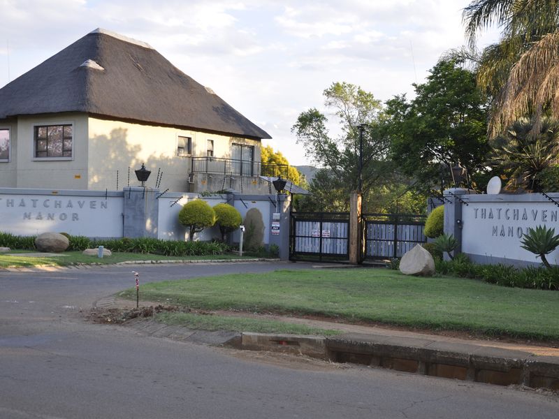 Front entrance view of Thatchaven Manor featuring a distinctive thatch roof, secure perimeter wall with electric fencing, and gated access.