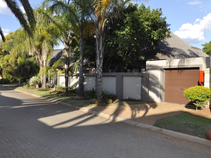 Front view of the property featuring a thatched roof, secure boundary wall, and a private paved driveway with an integrated garage.