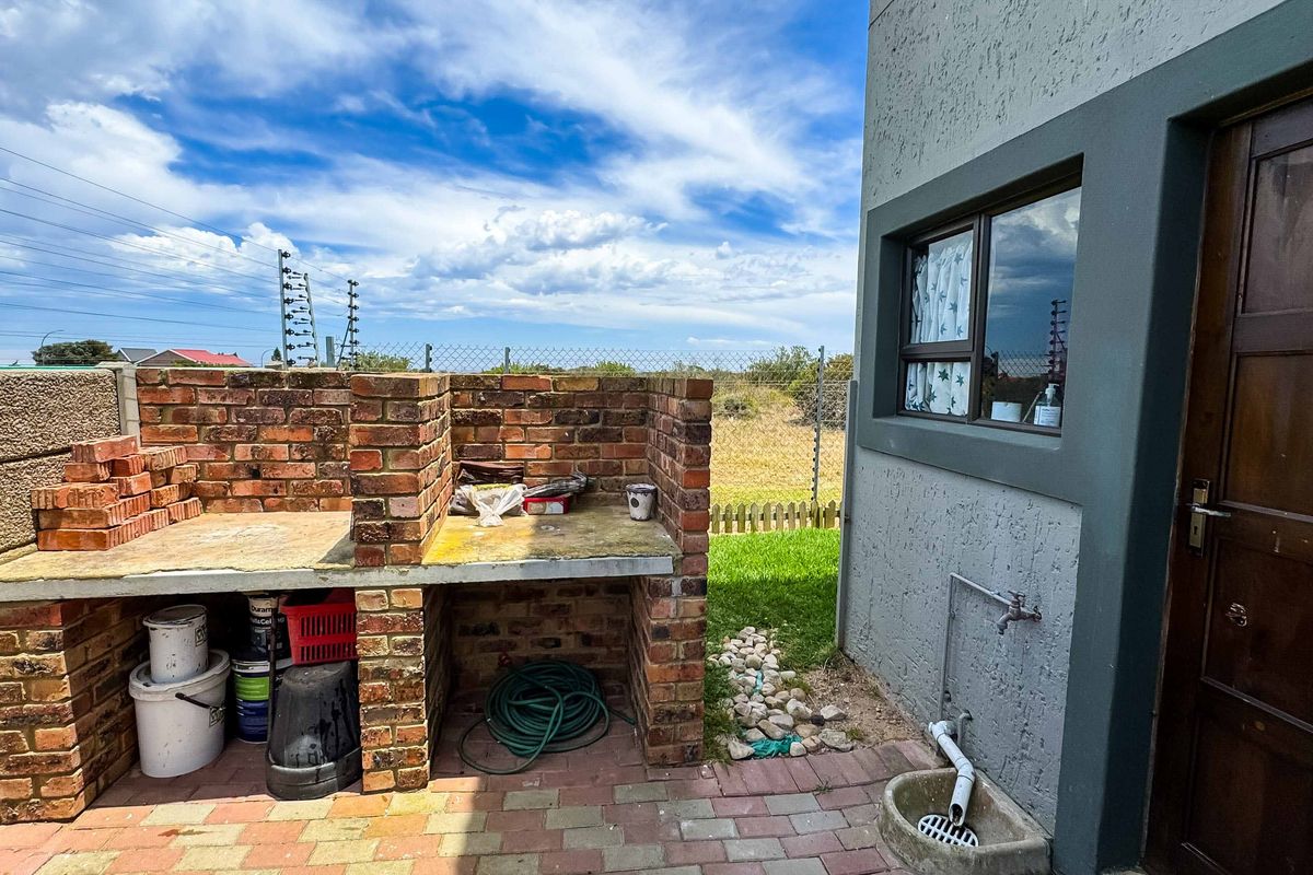 Outdoor area featuring a built-in brick braai, paved flooring, and an external water tap with a small drainage basin.