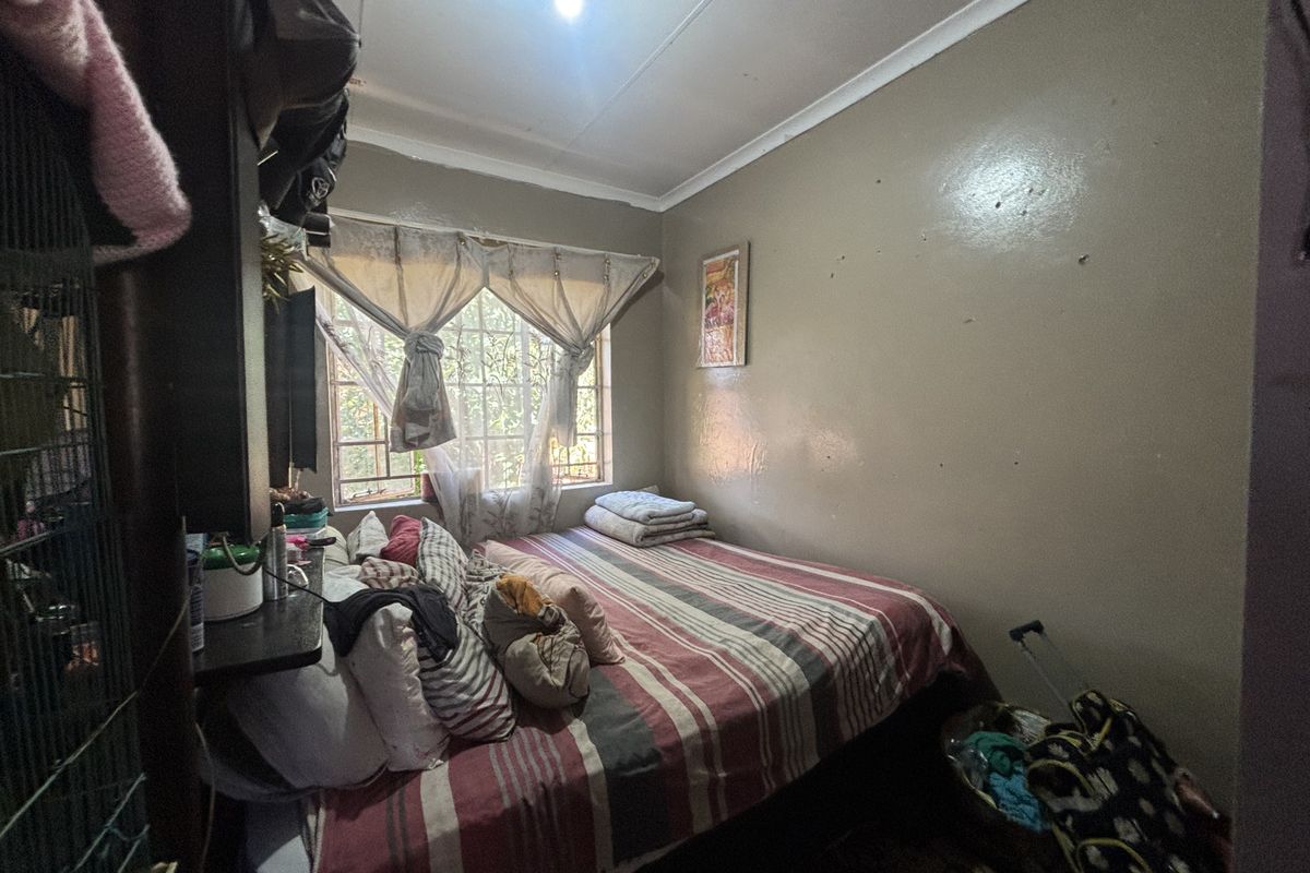 A compact bedroom featuring a window with security bars and standard interior finishes, requiring cosmetic updates to improve the overall aesthetic.