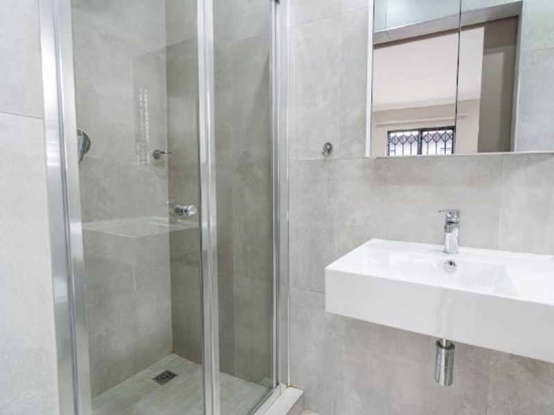 Modern bathroom featuring a glass shower enclosure, wall-mounted basin with chrome fixtures, and a mirrored medicine cabinet with neutral grey wall tiling.