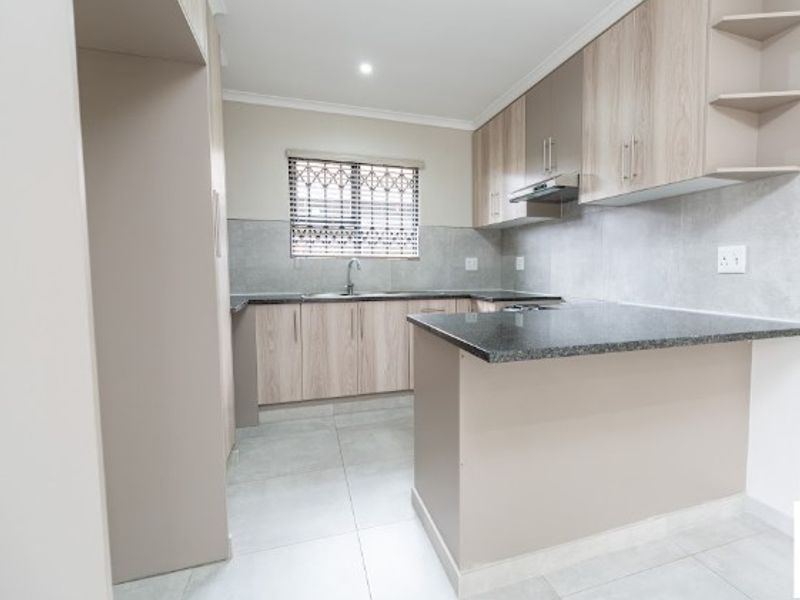 Modern kitchen featuring light wood-finish cabinetry, granite countertops, tiled backsplash, and integrated extractor fan in a clean, neutral space.