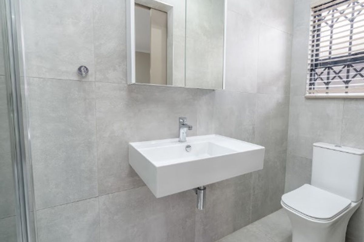 Modern bathroom featuring a wall-mounted basin, mirrored medicine cabinet, dual-flush toilet, and a glass shower enclosure with neutral grey tiling throughout.