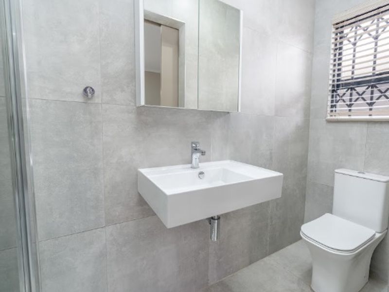 Modern bathroom featuring a wall-mounted basin, mirrored medicine cabinet, dual-flush toilet, and a glass shower enclosure with neutral grey tiling throughout.