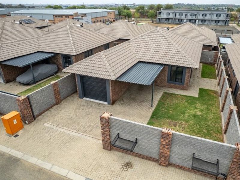 Aerial view of a residential property featuring a tiled roof, paved driveway, single garage, carport, and a private garden area with perimeter walling.