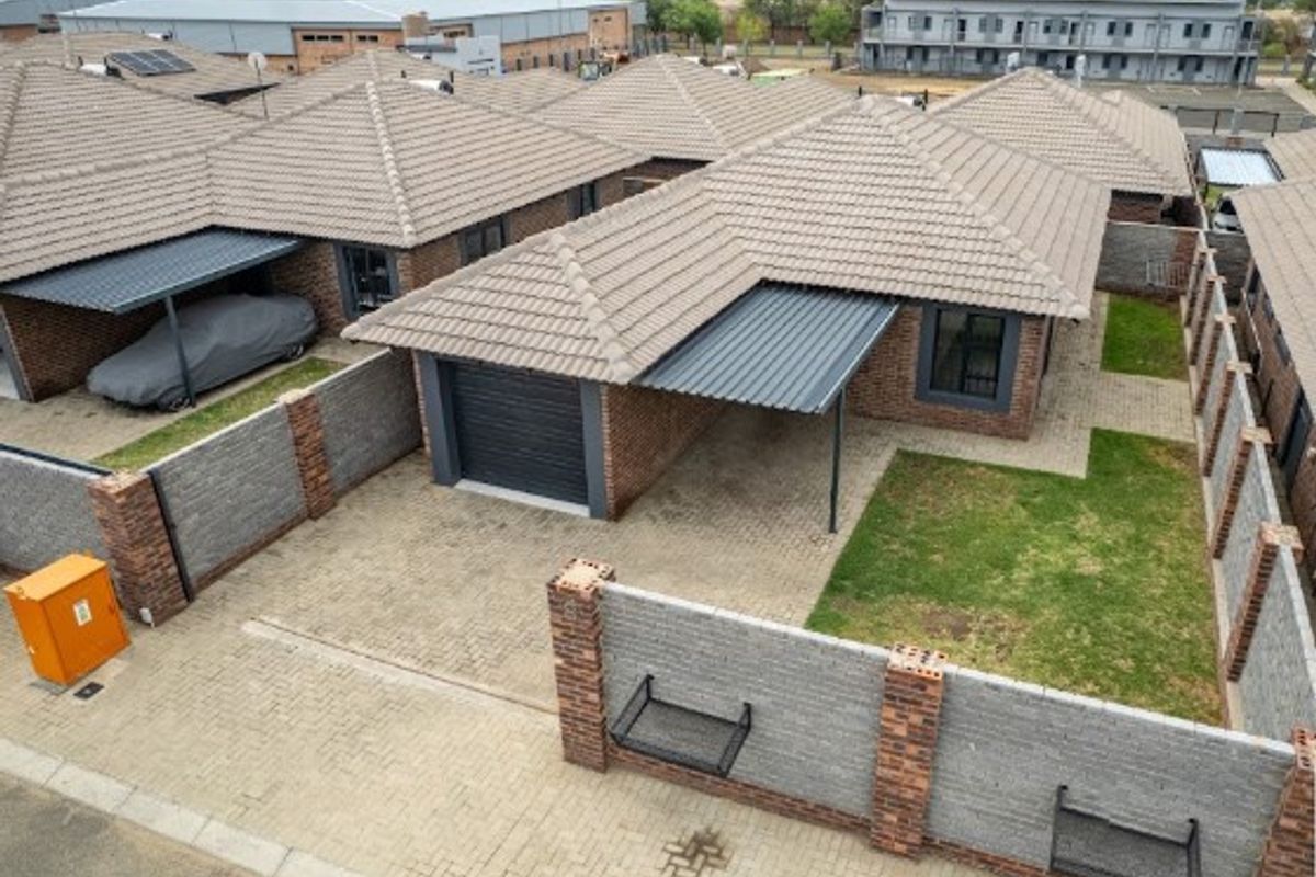 Aerial view of a residential property featuring a tiled roof, paved driveway, single garage, carport, and a private garden area with perimeter walling.