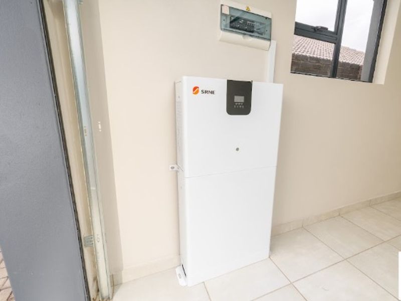 A clean utility space featuring a wall-mounted solar inverter and an electrical distribution board, finished with neutral tiled flooring.