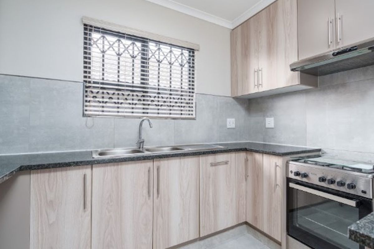 Modern kitchen featuring light wood-finish cabinetry, granite countertops, stainless steel appliances, and a tiled backsplash with a secure window.