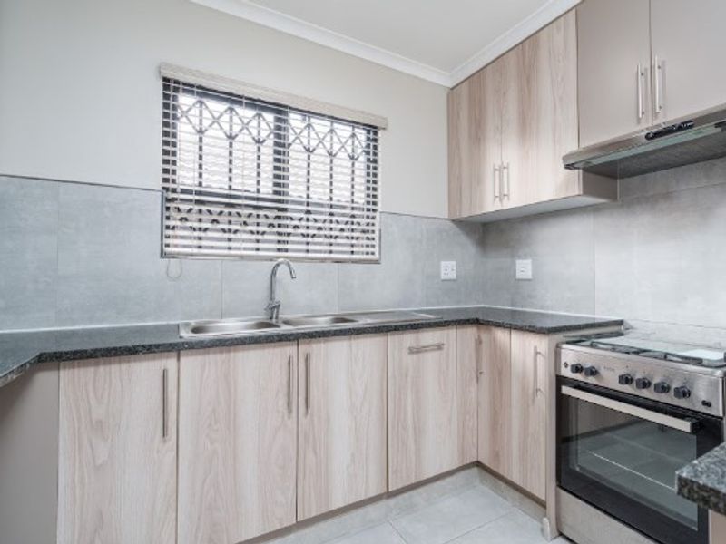 Modern kitchen featuring light wood-finish cabinetry, granite countertops, stainless steel appliances, and a tiled backsplash with a secure window.