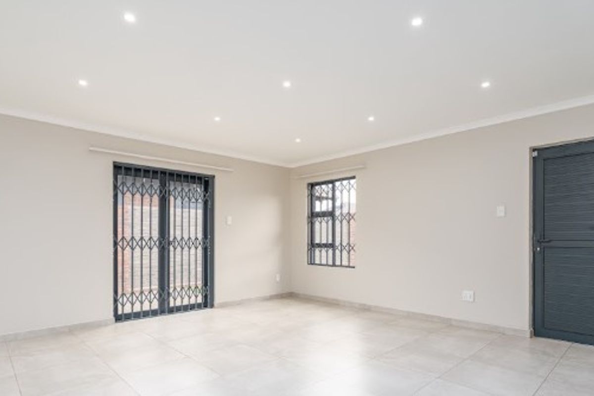 A bright, empty living area featuring neutral tiled flooring, recessed downlighting, and secure access points with fitted security gates and bars.