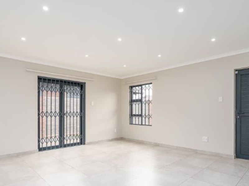 A bright, empty living area featuring neutral tiled flooring, recessed downlighting, and secure access points with fitted security gates and bars.