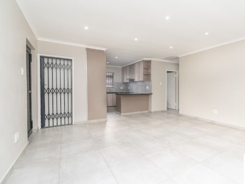 Spacious open-plan living area featuring neutral tiled flooring, recessed lighting, and a modern kitchen with built-in cabinetry and a breakfast island.