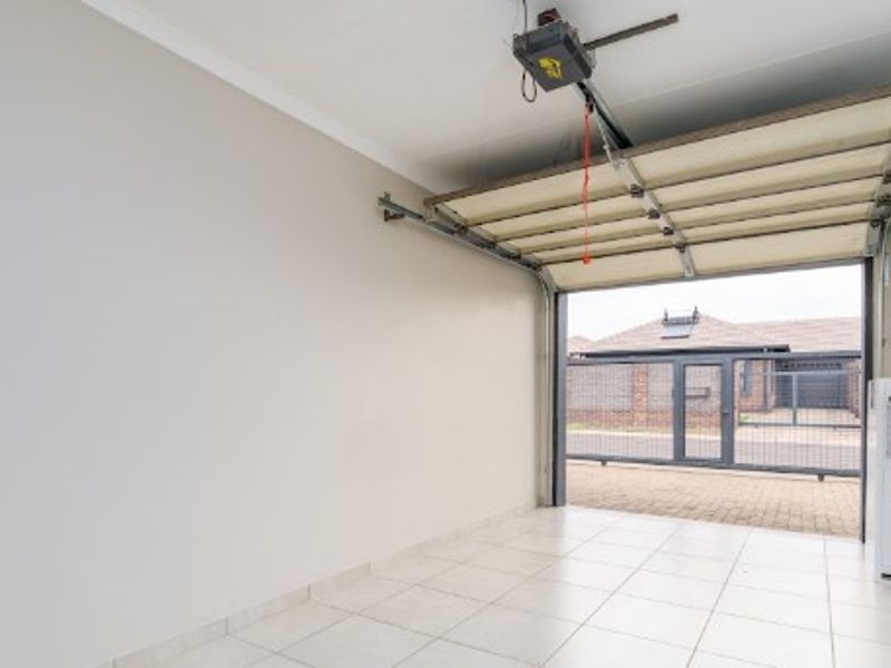 A clean, empty garage featuring tiled flooring, a sectional overhead door with an automated motor, and a side window.