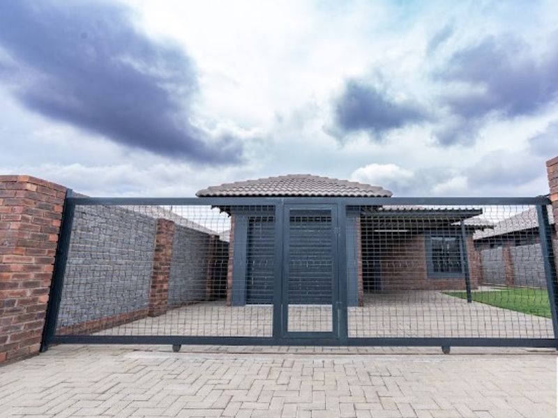 Front view of a modern house featuring a paved driveway, secure sliding metal gate, and brick boundary walls with a tiled roof.