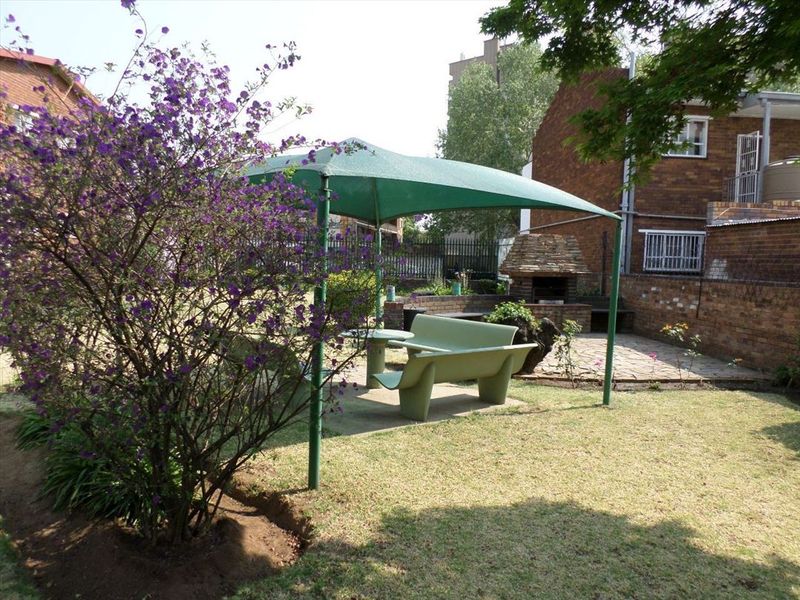 A private garden area featuring a paved patio, a built-in brick braai, and a shade sail structure for outdoor entertainment.