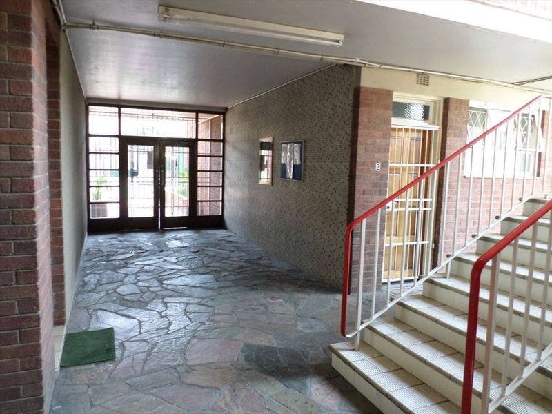 A communal entrance area featuring stone flooring, brick wall accents, and a staircase with a metal handrail leading to the upper levels.