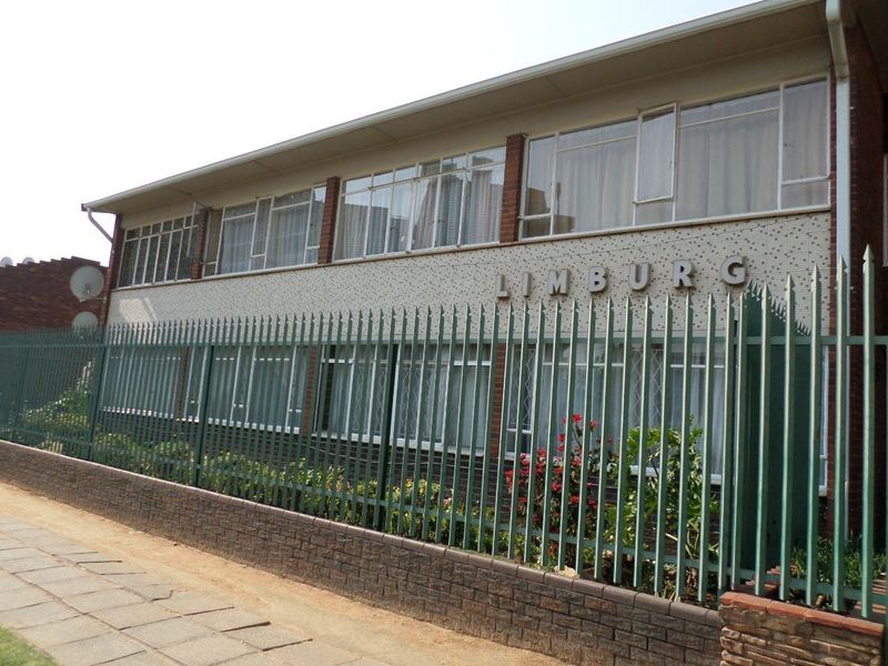 Front exterior view of the Limburg apartment building, featuring a brick and tiled facade with secure metal perimeter fencing.