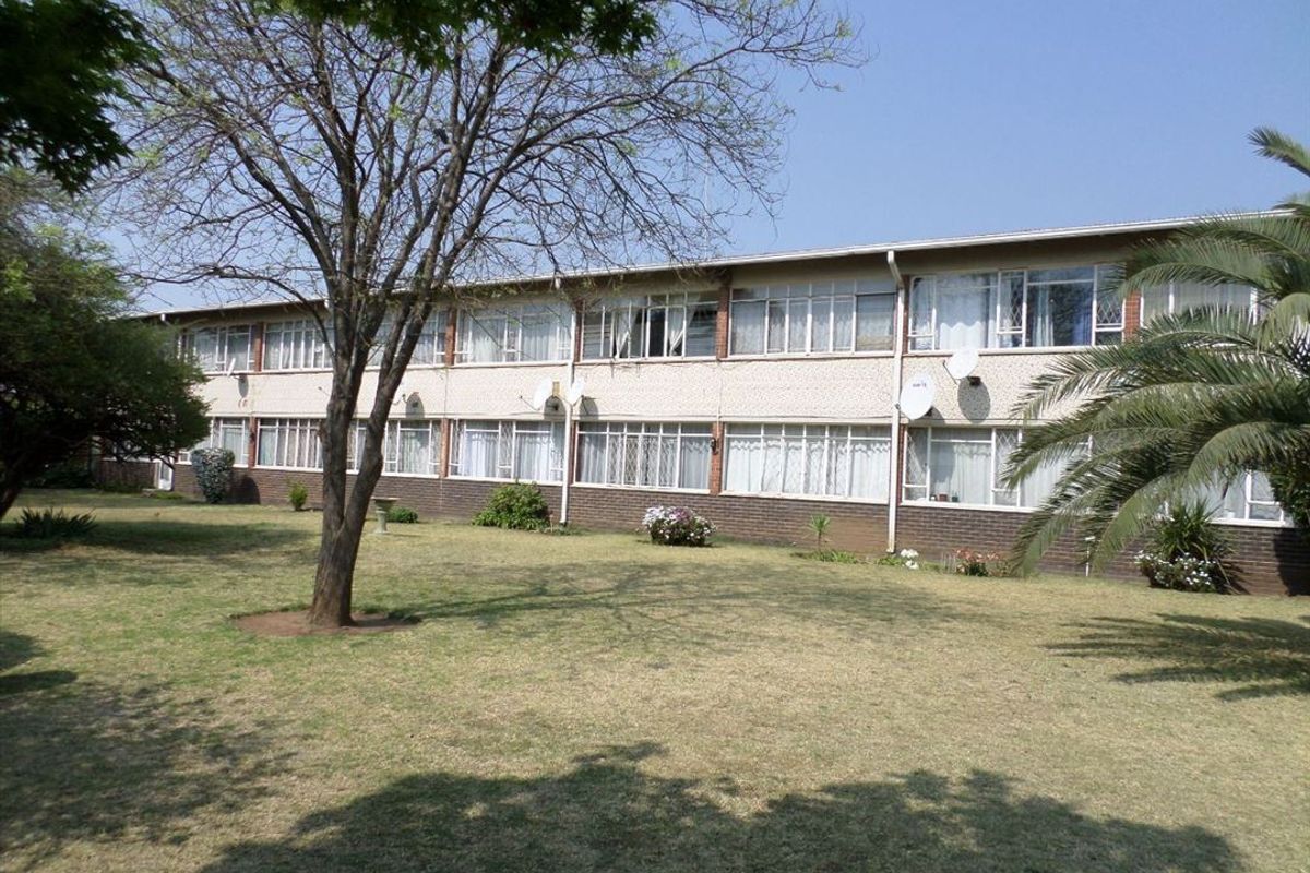 A view of the rear elevation of a multi-story flat complex featuring brick exterior walls, large windows, and a well-maintained communal garden area.