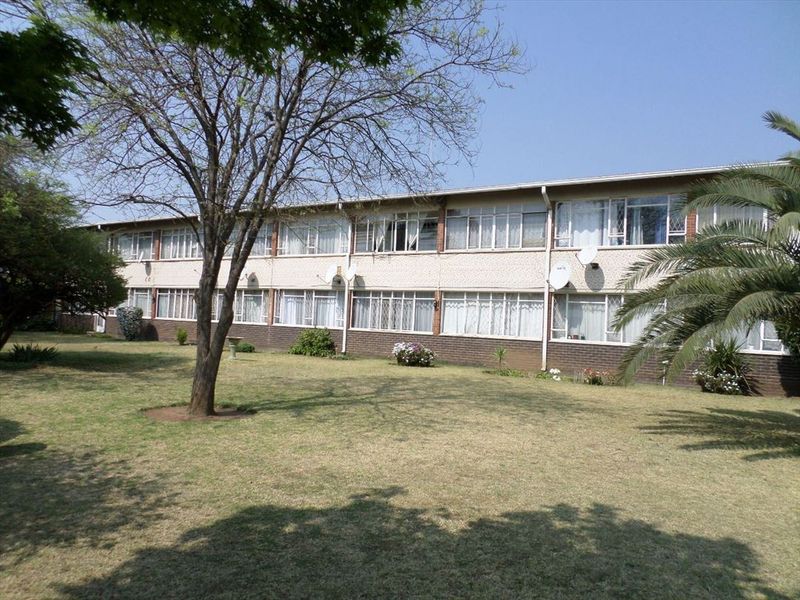 A view of the rear elevation of a multi-story flat complex featuring brick exterior walls, large windows, and a well-maintained communal garden area.