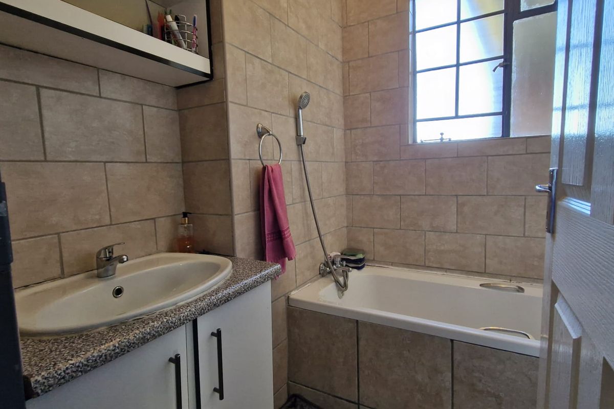 A functional bathroom featuring a built-in vanity with basin, a bathtub with handheld shower attachment, and neutral wall tiling.