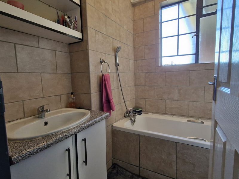 A functional bathroom featuring a built-in vanity with basin, a bathtub with handheld shower attachment, and neutral wall tiling.