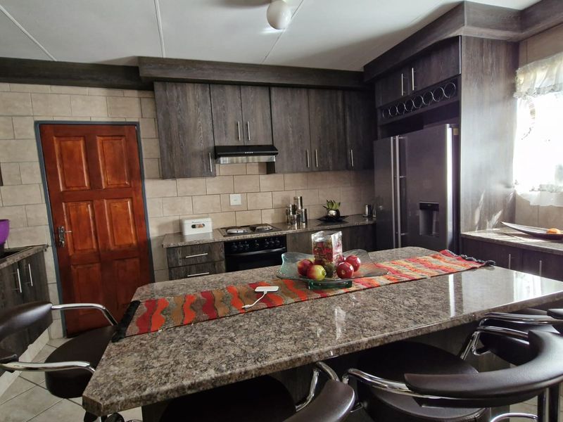 A functional kitchen featuring dark wood cabinetry, a large granite-topped island, tiled backsplash, and built-in cooking appliances.