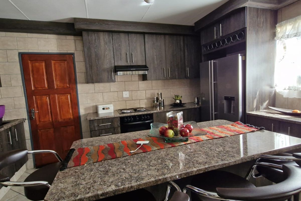 A functional kitchen featuring dark wood cabinetry, a large granite-topped island, tiled backsplash, and built-in cooking appliances.
