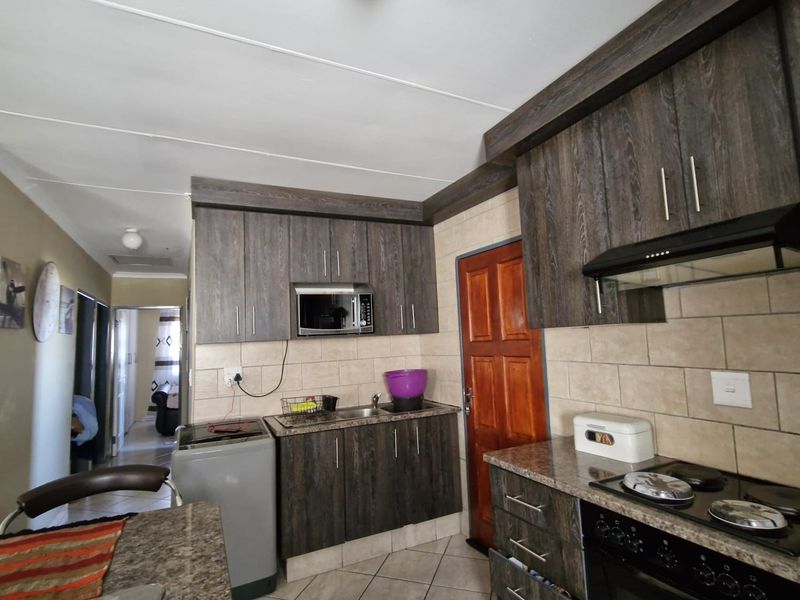 A functional kitchen featuring dark wood-grain cabinetry, granite countertops, a built-in oven with extractor fan, and tiled flooring.