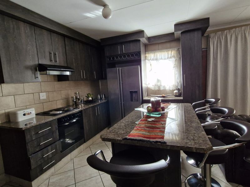 Modern kitchen featuring dark wood cabinetry, granite countertops, a central island with breakfast bar seating, and integrated appliances.