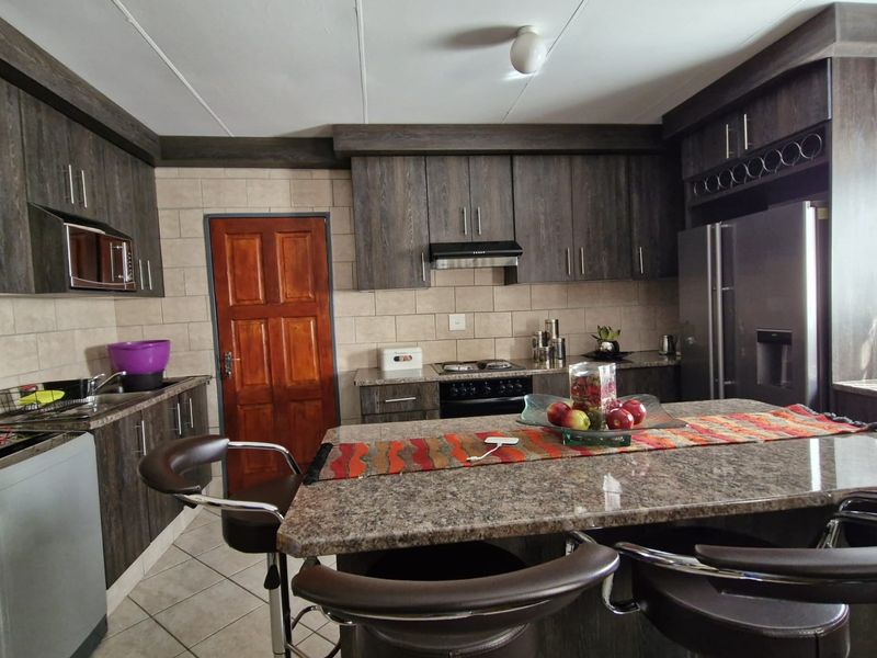A functional kitchen featuring dark wood cabinetry, granite countertops, a central island, and tiled finishes throughout.