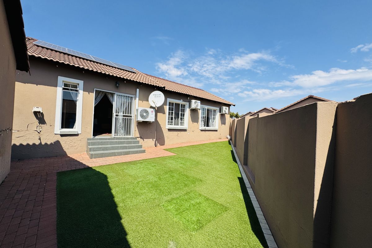 Rear exterior view of the townhouse featuring a private garden with artificial lawn, paved walkway, and boundary wall.
