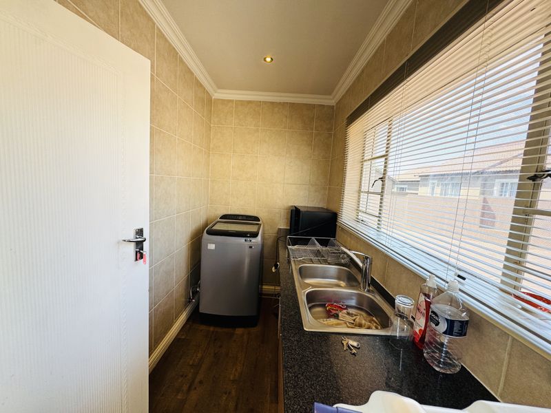 A functional laundry room featuring tiled walls, a double stainless steel sink with mixer tap, laminate countertop, and venetian blinds.