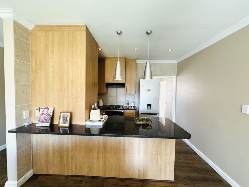 Modern kitchen featuring wood veneer cabinetry, granite countertops, a breakfast bar, and integrated appliances with a neutral tiled backsplash.