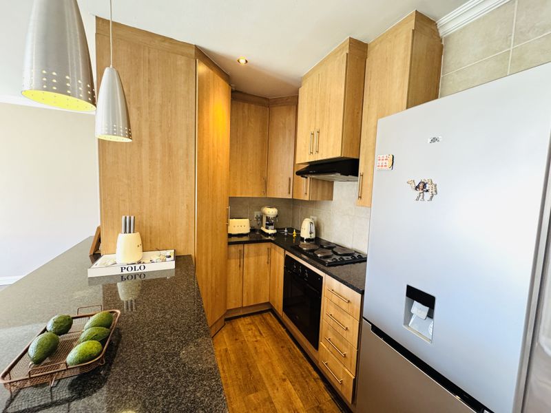 A functional kitchen featuring light wood cabinetry, granite countertops, a built-in oven, electric hob, and a breakfast bar area.