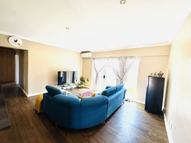 A well-maintained living room featuring laminate flooring, recessed lighting, a split-system air conditioner, and a sliding glass door providing access to the exterior.