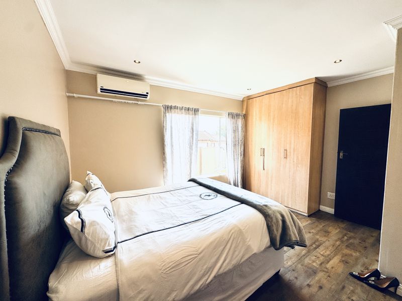 A well-maintained bedroom featuring laminate flooring, built-in wooden wardrobes, recessed lighting, and a wall-mounted air conditioning unit.