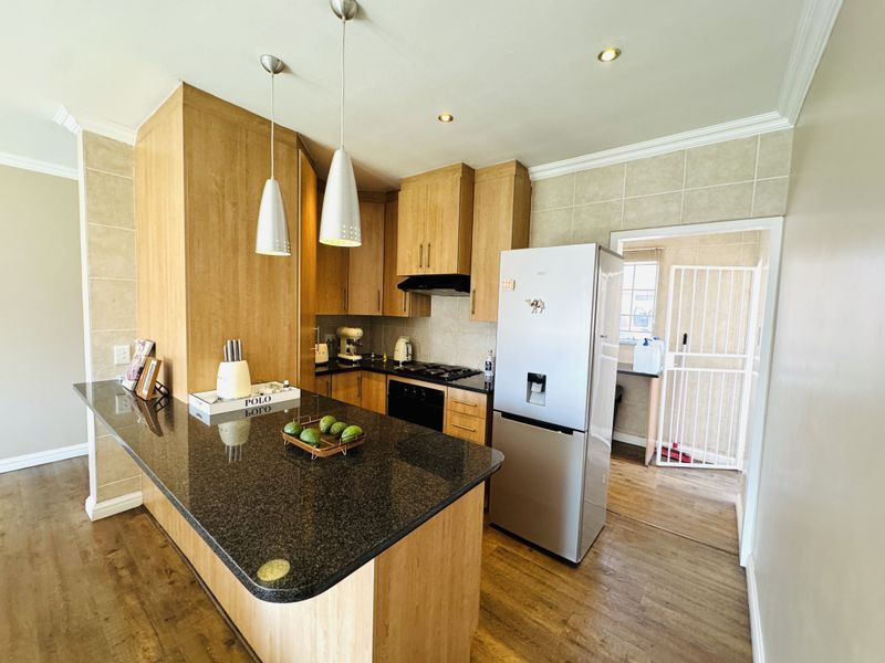 A well-maintained kitchen featuring granite countertops, wooden cabinetry, built-in appliances, and pendant lighting, with an adjacent scullery area visible through the doorway.