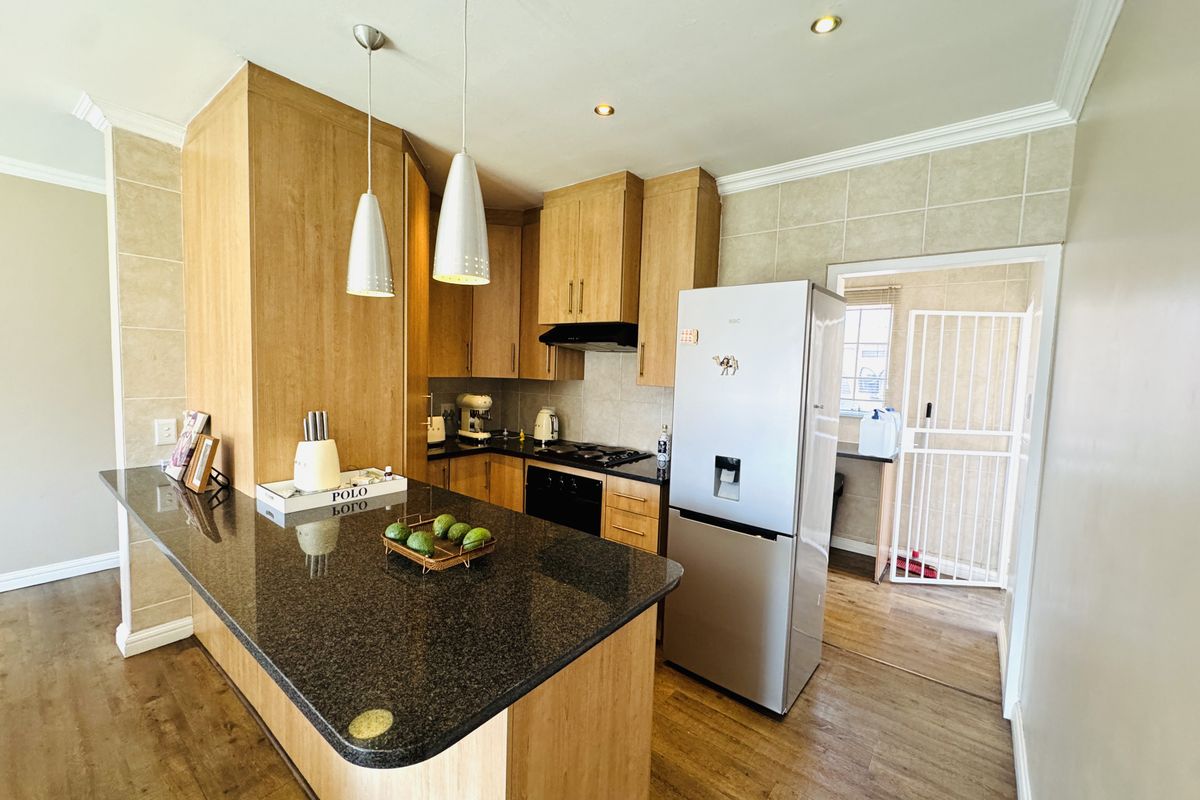A well-maintained kitchen featuring granite countertops, wooden cabinetry, built-in appliances, and pendant lighting, with an adjacent scullery area visible through the doorway.