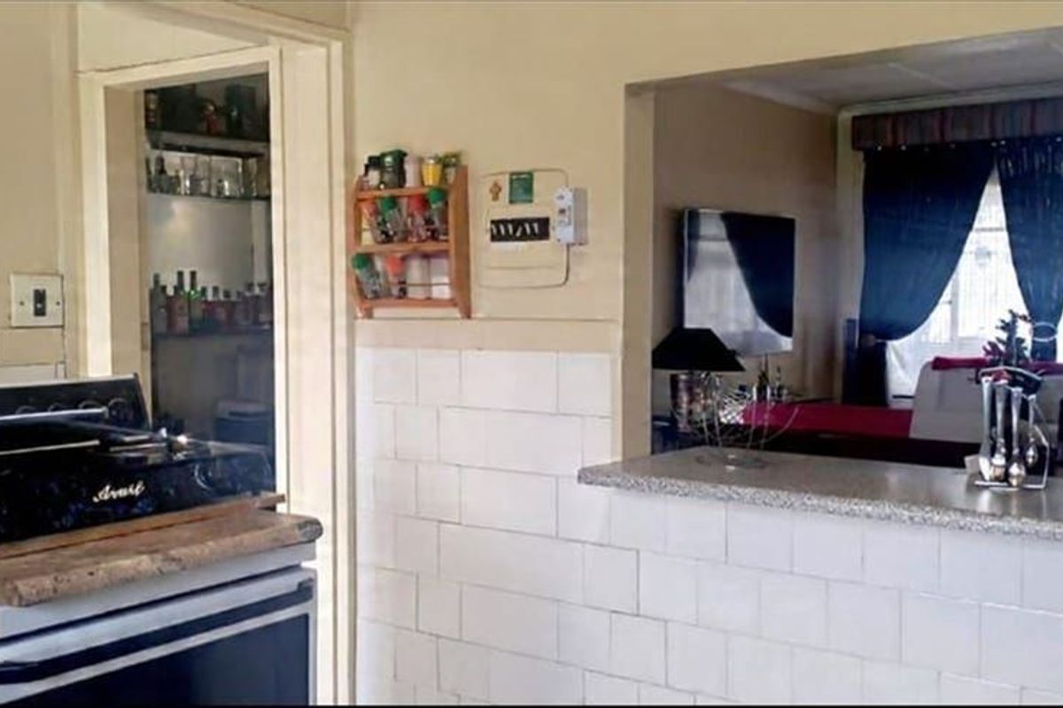 A dated kitchen featuring a breakfast bar pass-through to the living area, tiled splashbacks, and a freestanding stove.