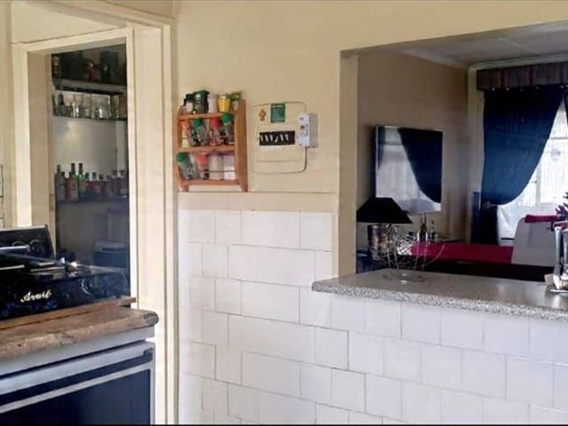 A dated kitchen featuring a breakfast bar pass-through to the living area, tiled splashbacks, and a freestanding stove.