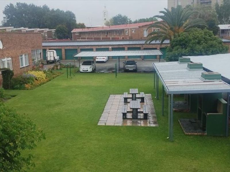 An elevated view of a communal garden area featuring a paved patio with braai facilities and covered parking bays for residents.