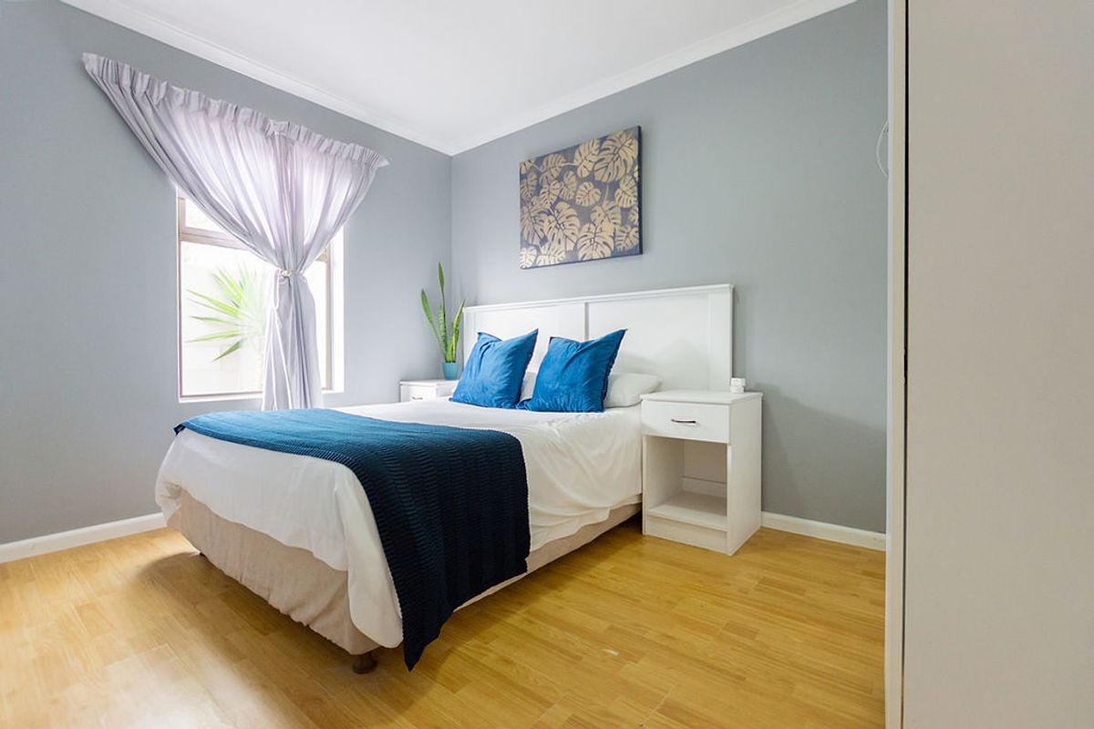 A well-maintained bedroom featuring light wood-look flooring, neutral grey walls, and a built-in cupboard, offering a clean and comfortable living space.